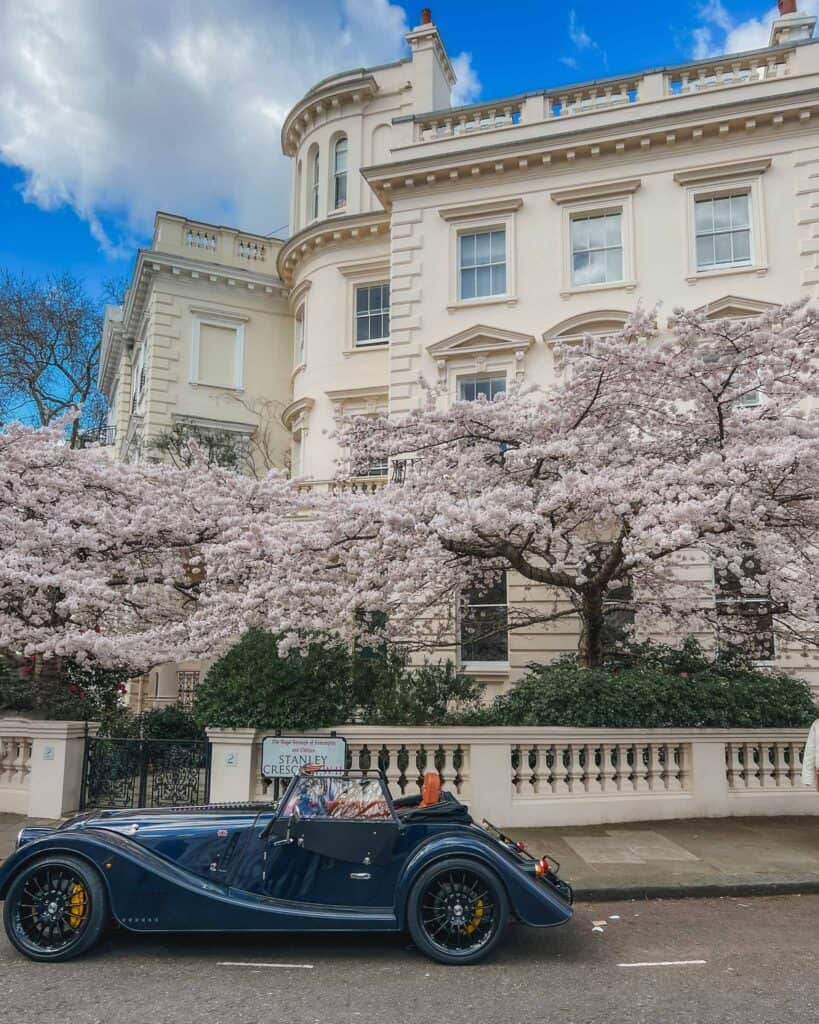 Stanley Crescent in Kensington is quite an iconic street in London. This neighborhood is known for its grand, period architecture, featuring a mix of styles from Georgian and Victorian to modern. On this corner you'll find stucco facades intricated with curved buildings and adorning detail around the windows and perimeters. In the spring, there is the most beautiful cherry blossom trees that bloom in front of this beautiful cream building, the white and pink hues of the trees create a perfect backdrop for a photo, especially when you add a resident's antique car in as well!