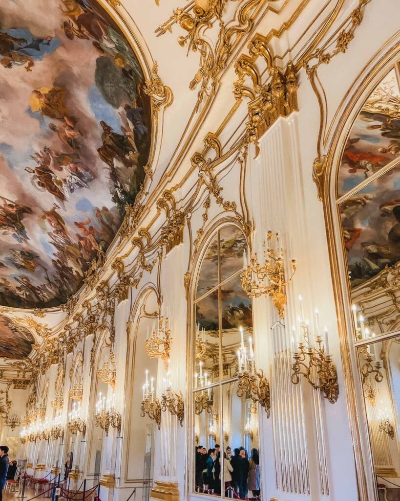 This is the Great Gallery at The Habsburg Schonbrunn Palace which features a long, rectangular room with elaborate chandeliers, gold accents, and ceiling frescoes that create the ambience of a true fairytale.