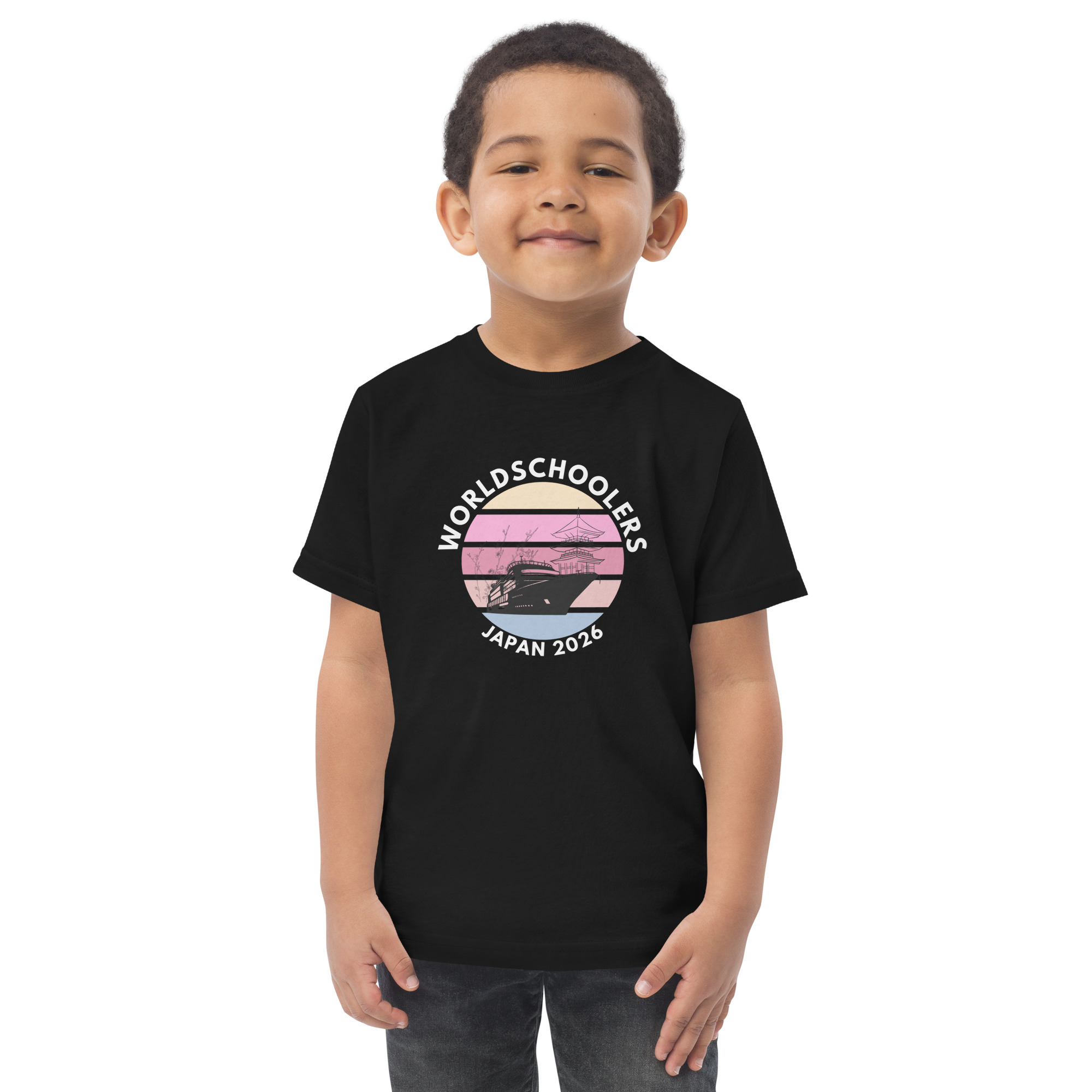 Adorable toddler wearing a black jersey T-shirt with "World Schoolers Japan 2026" graphic, featuring a sunset and airplane design, perfect for travel-themed kids' apparel.