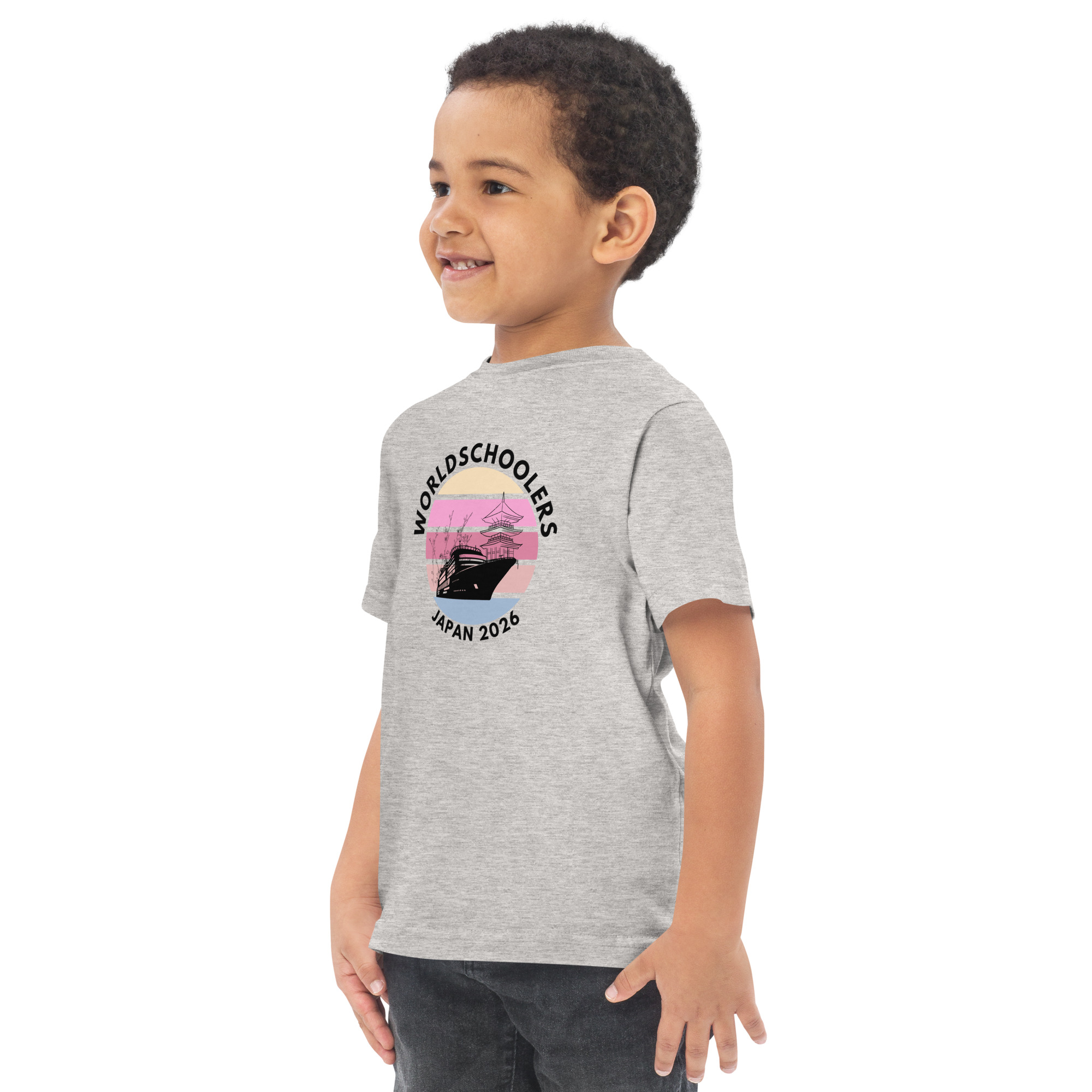 Toddler wearing a grey jersey T-shirt with "World Schoolers Japan 2026" graphic, featuring a ship and pink sunset, perfect for travel-themed kids' apparel.