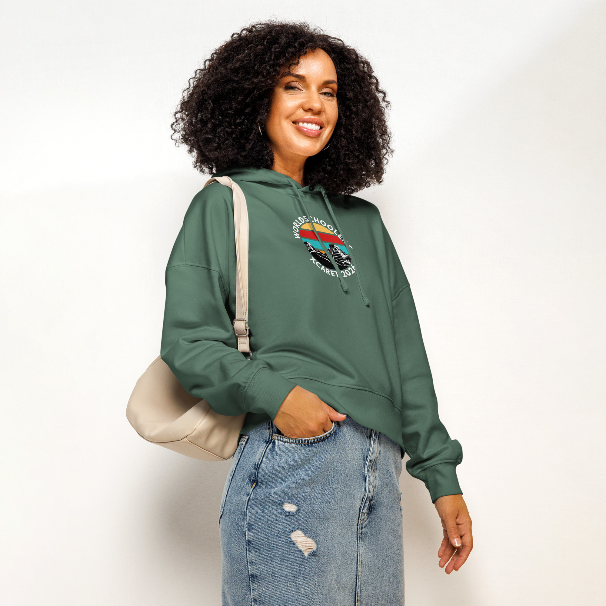 Woman wearing a green Xcaret 2026 organic hoodie with a colorful graphic, paired with distressed jeans, showcasing casual comfort and eco-friendly fashion.