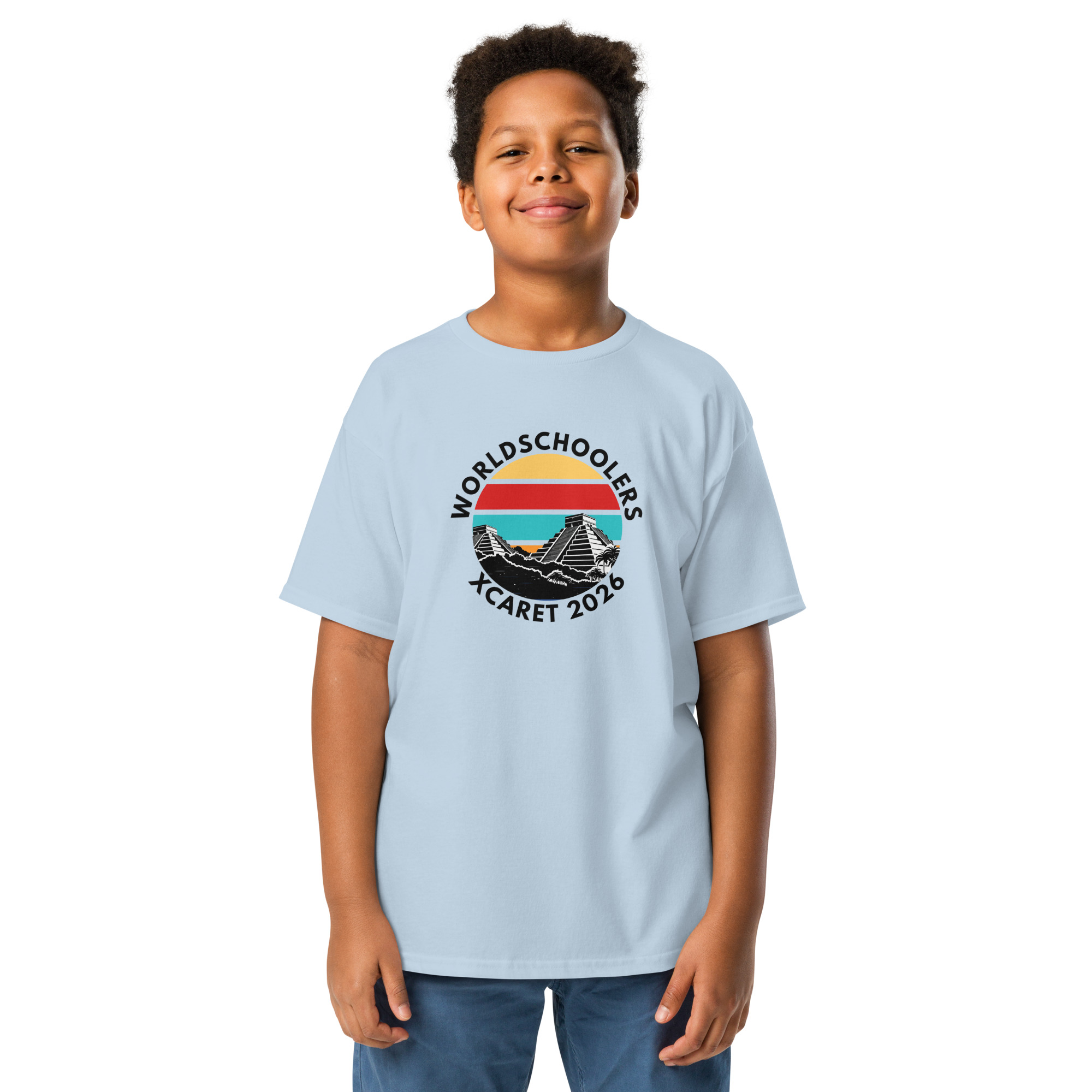Child wearing a light blue Xcaret 2026 youth graphic tee with mountain and sunset design, perfect for travel and adventure-themed apparel.