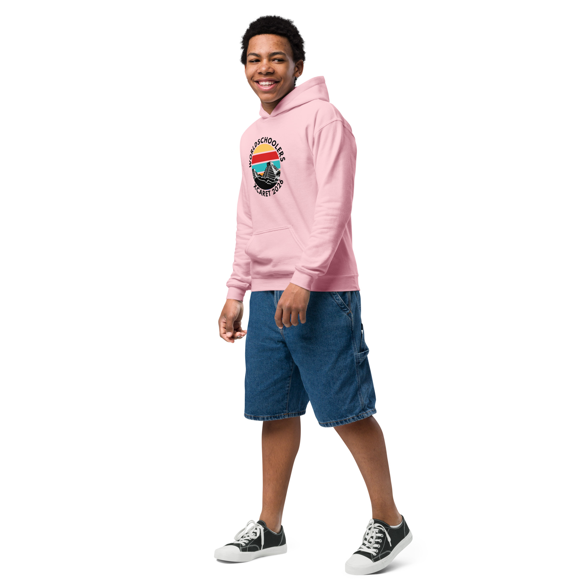Youth wearing pink Xcaret 2026 themed hoodie with graphic design, casual denim shorts, and sneakers, showcasing comfortable and stylish youth apparel for travel and adventure.