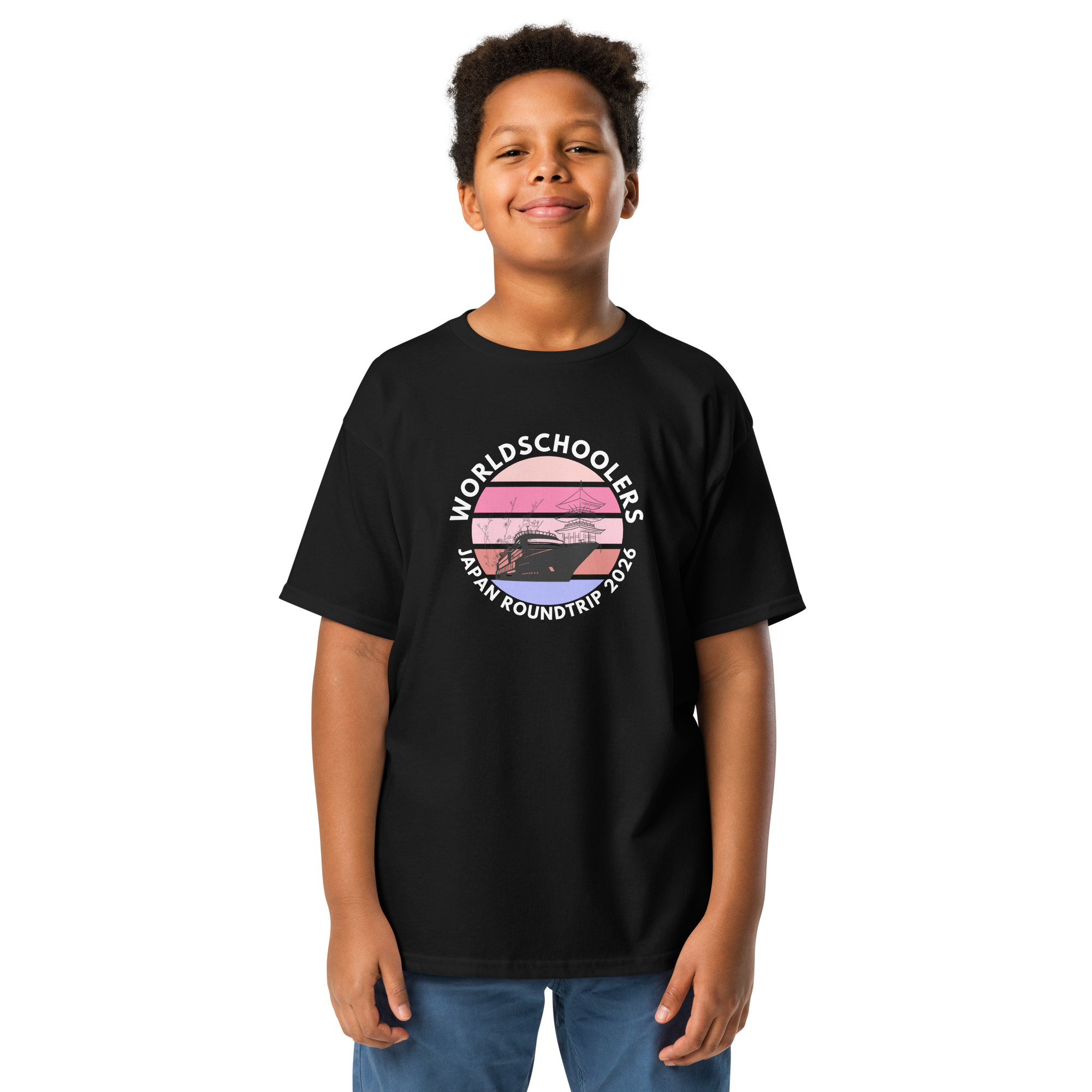 Child wearing a black "World Schoolers Japan Roundtrip 2026" graphic tee, showcasing a colorful sunset design with mountains and trees. Perfect for travel-themed youth apparel.