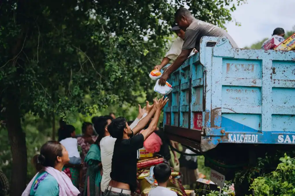 Two men handing groceries to villagers from a truck in Nepal