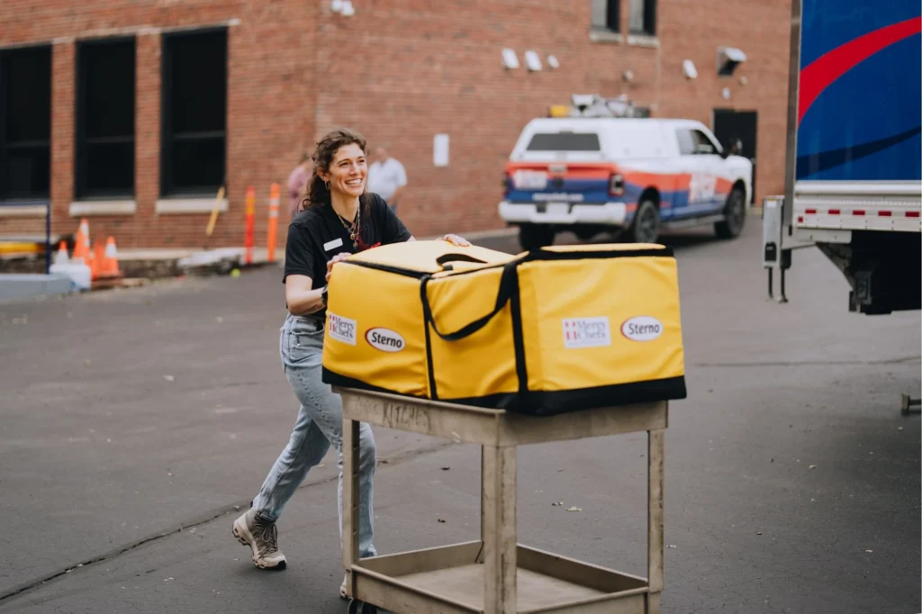 A Mercy Chefs staff member pushes a cart with hot meals in Sterno bags