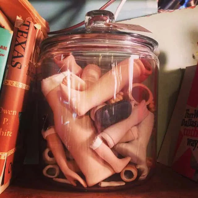 Glass jar filled with vintage doll limbs and parts for antique collection.