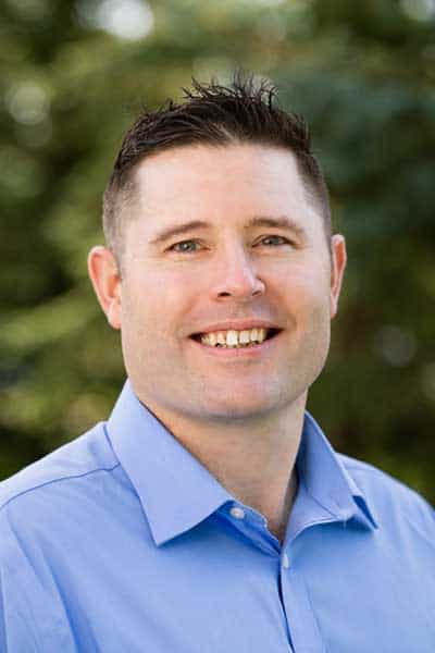 MHP, healthcare professional, smiling man in blue shirt outdoors.