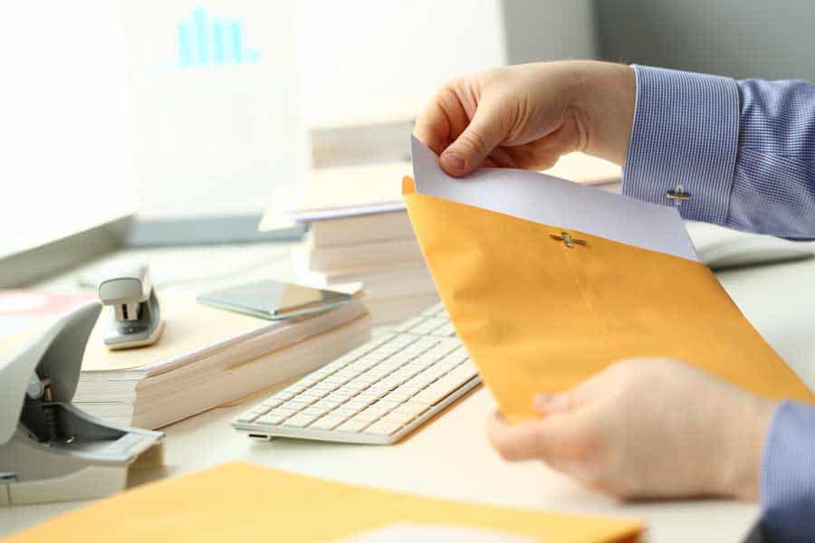Office worker handling a document at a desk with computer and office supplies.