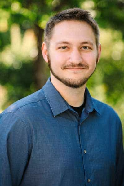 Professional headshot of a young man outdoors, representing mental health and wellness services.