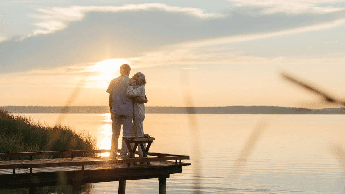 Sunset scene featuring a couple embracing on a wooden dock by the lake at dusk.