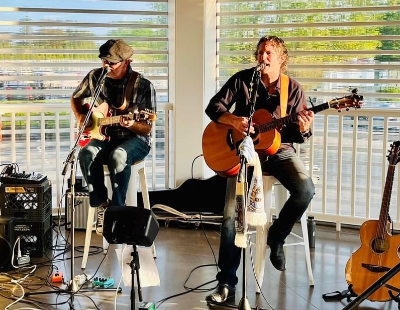 Two musicians perform with guitars in front of large windows at Michael's Harborside.