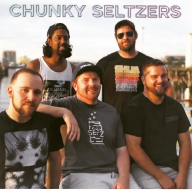 Group of five men outdoors with a city skyline in the background.