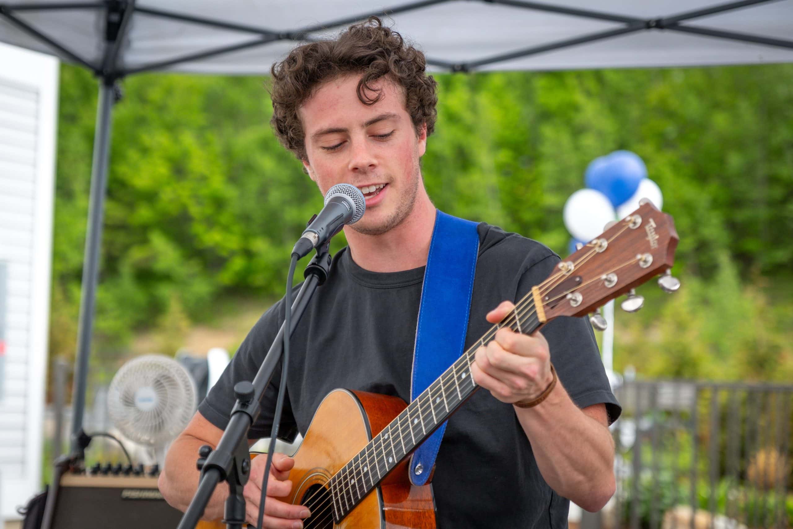 Young man singing and playing guitar outdoors at Michael's Harborside event.