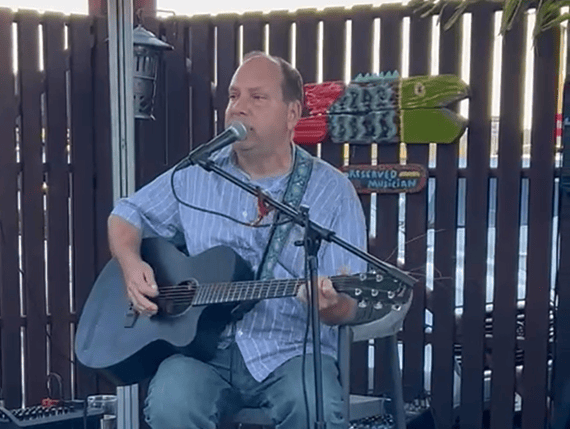 Musician playing guitar and singing at Michael's Harborside outdoor event.