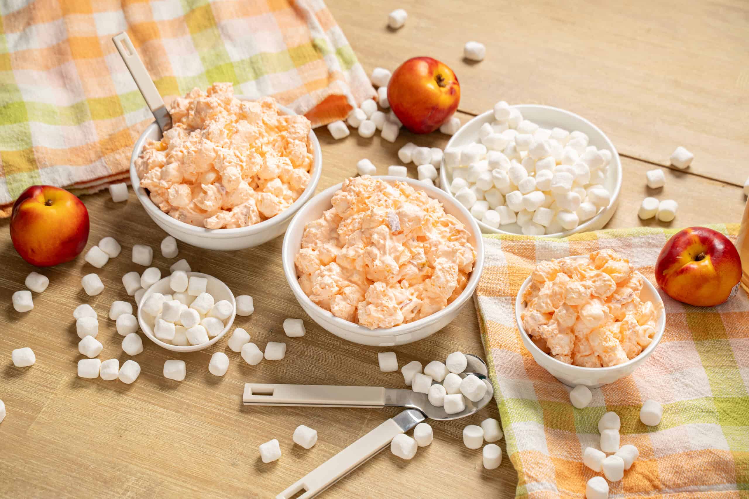 Fluffy homemade marshmallows in bowls with fresh apples on a wooden surface.