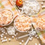 Fluffy marshmallow cream in bowls with fresh apples and marshmallows on a wooden table, colorful napkins, perfect for making sweet treats and desserts.