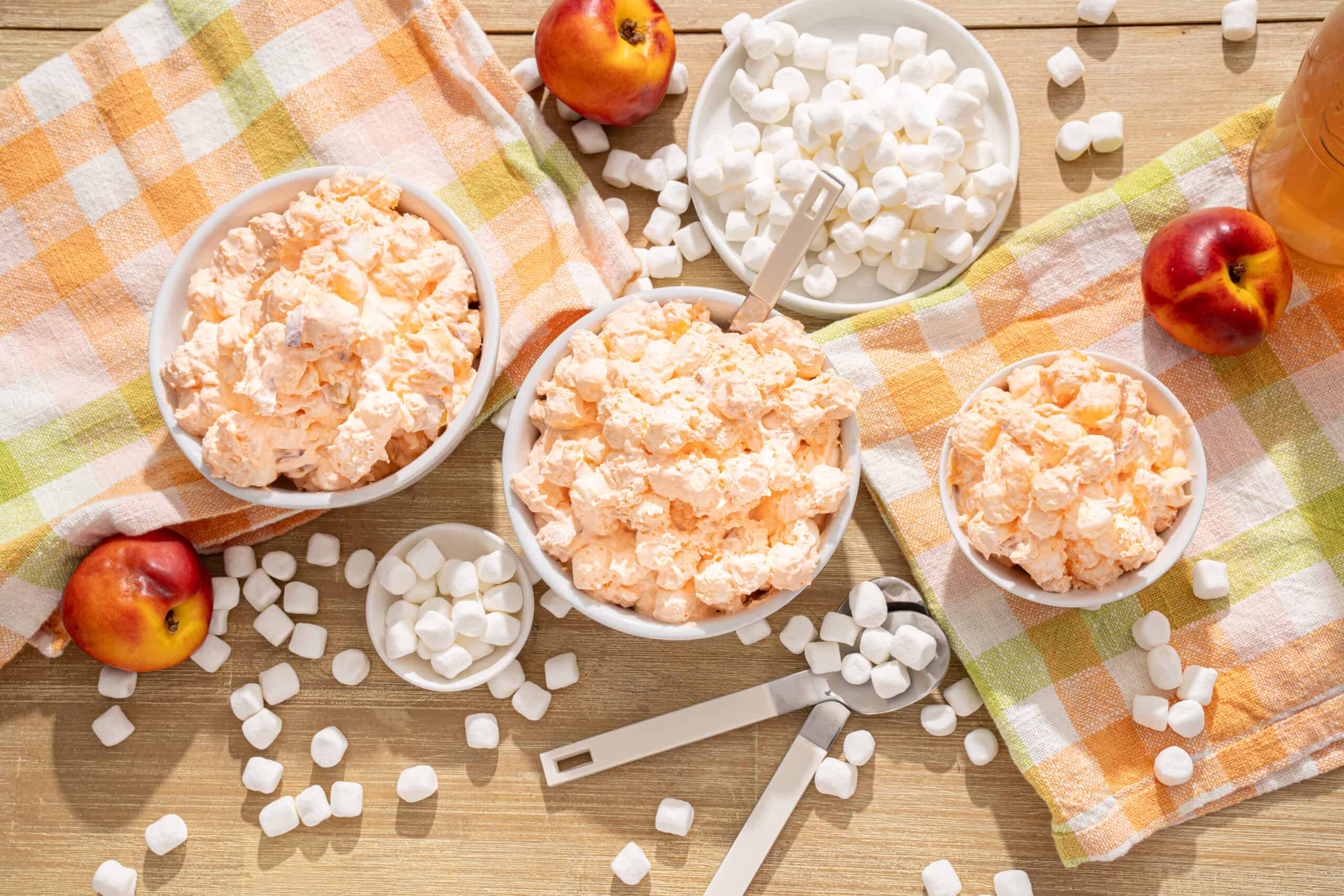 Fluffy marshmallow cream in bowls with fresh apples and marshmallows on a wooden table, colorful napkins, perfect for making sweet treats and desserts.