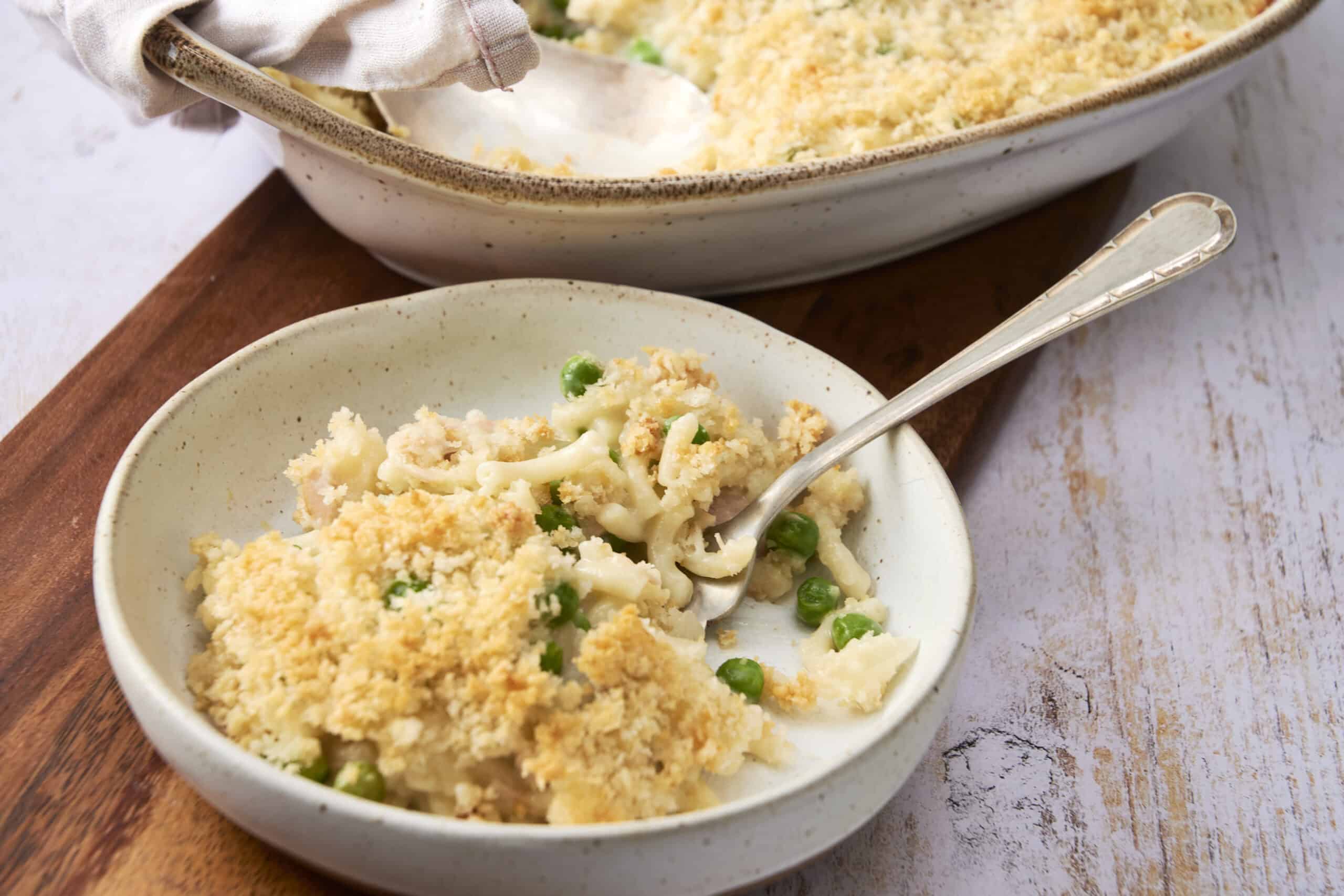 Creamy cauliflower casserole with peas and crispy breadcrumb topping served in a rustic white bowl, perfect for comforting side dishes and family dinners.