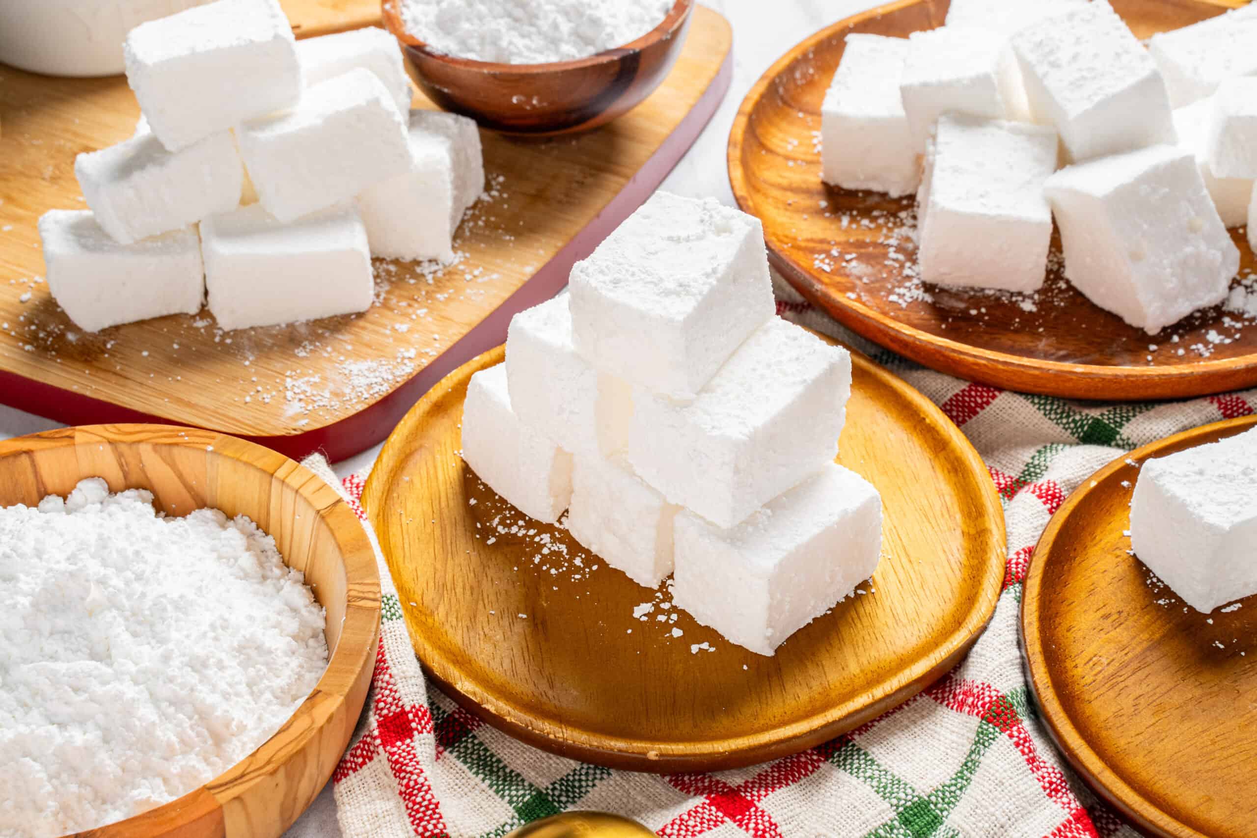Fresh white sugar cubes on rustic wooden plates and bowls, ready for baking or sweetening beverages, set on a colorful checkered cloth for a cozy kitchen scene.