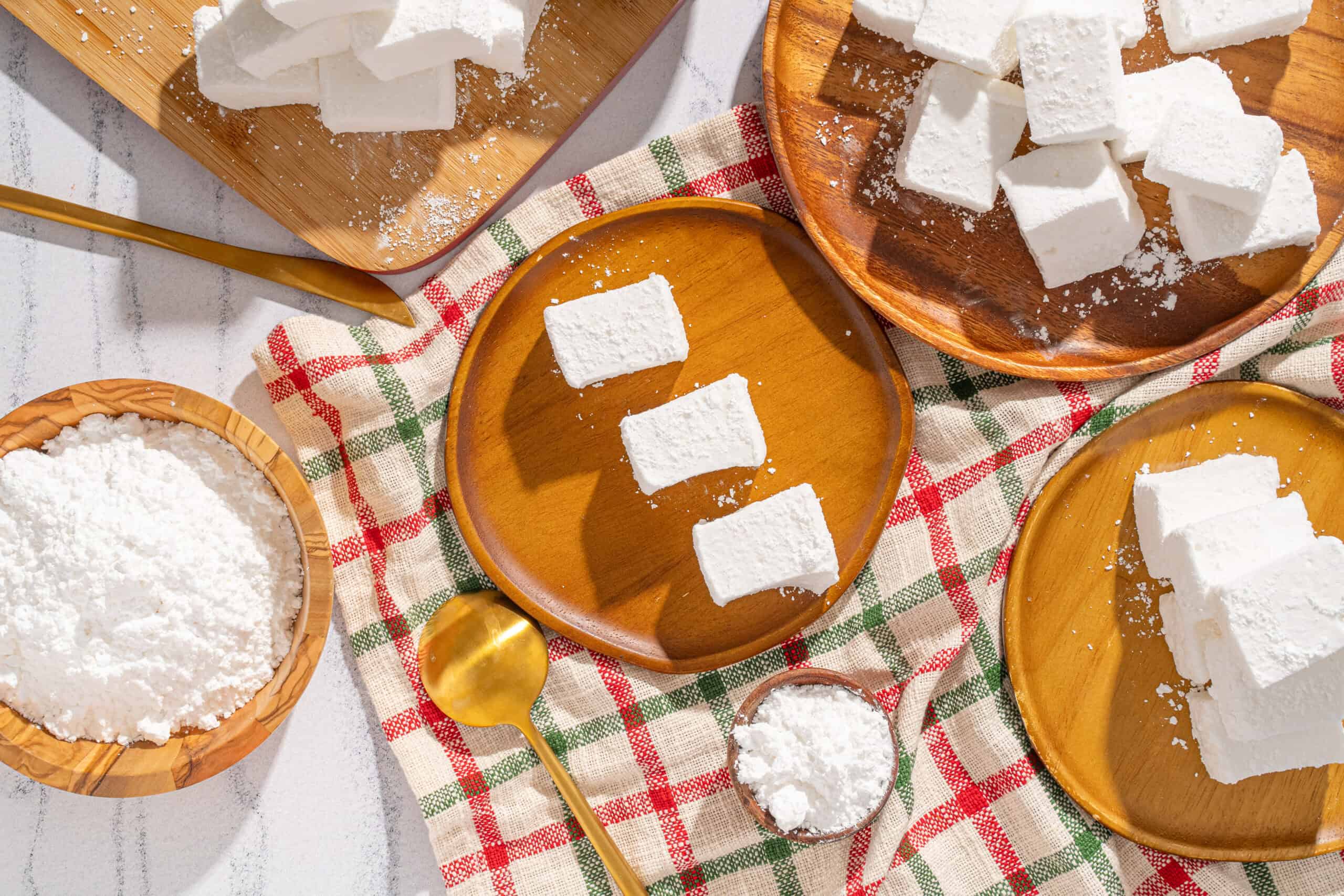 Cream cheese cubes on wooden and ceramic plates, with shredded cheese and a golden spoon, on a checkered tablecloth, perfect for cheese recipes and gourmet food presentation.
