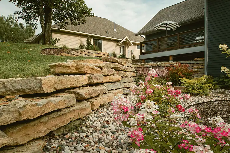 Stone retaining wall with landscaped garden and houses in the background.