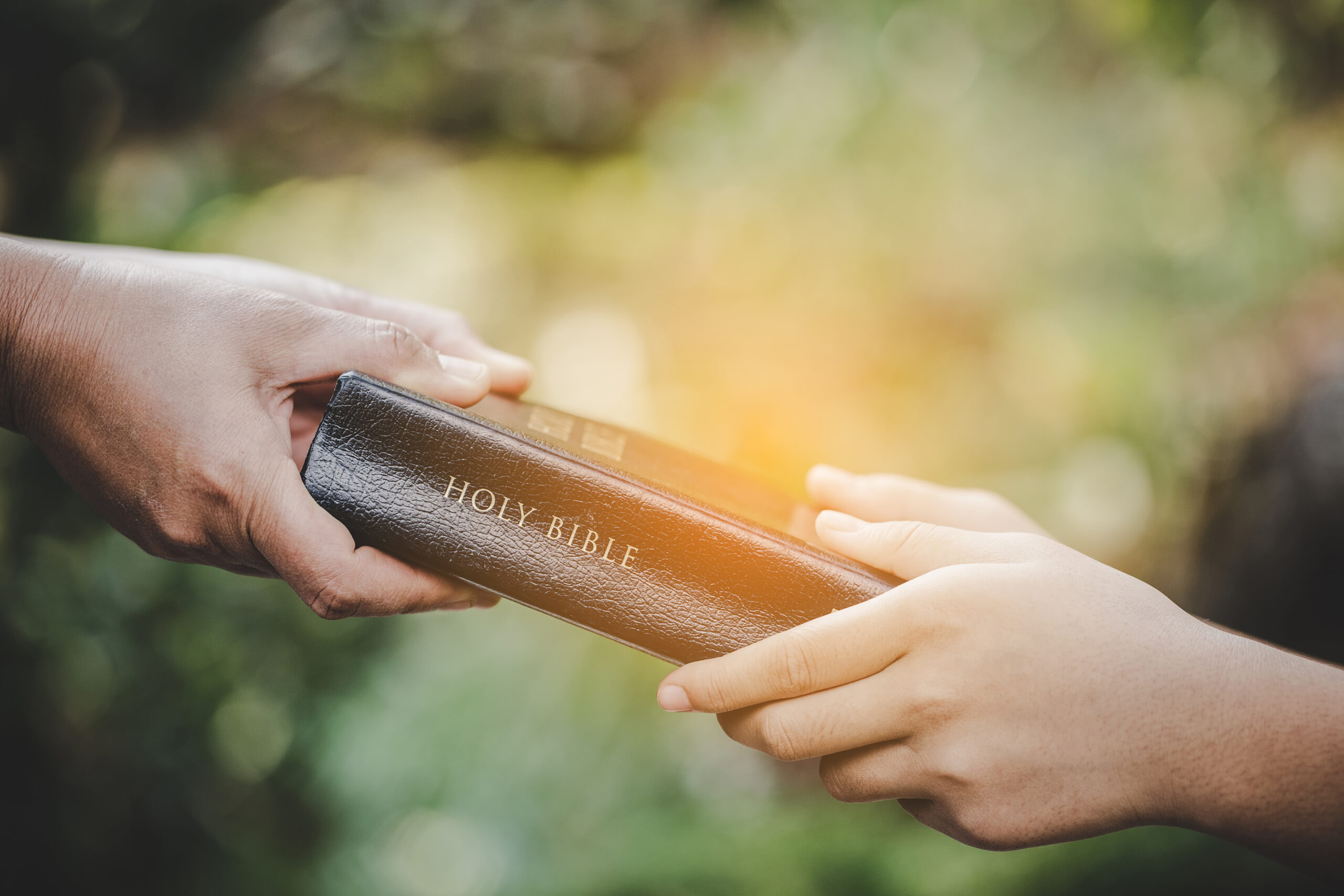 Closeup picture of male adulthood. Sharing the gospel to the you A person is handing a bible to another person through evangelism outreach.