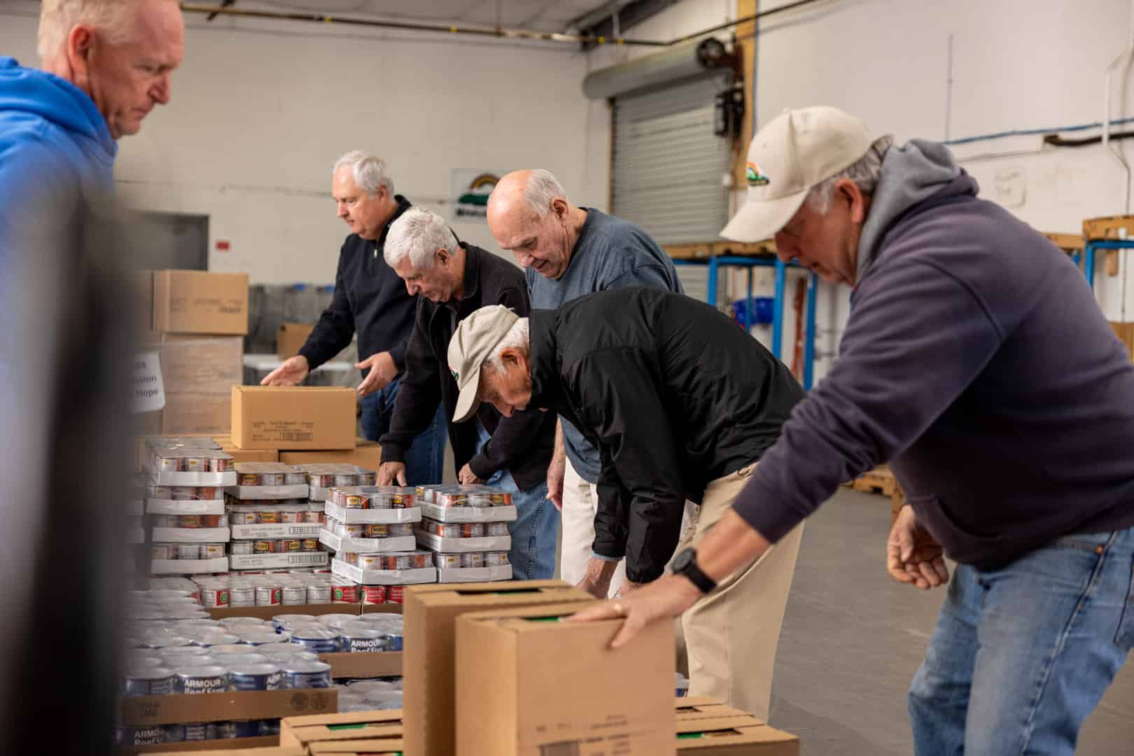 A group of men are putting food into boxes in a warehouse.
