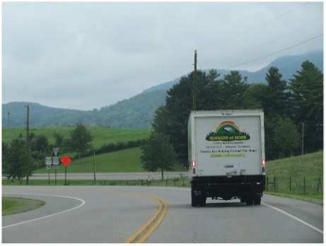 A truck driving down a country road with mountains in the background.