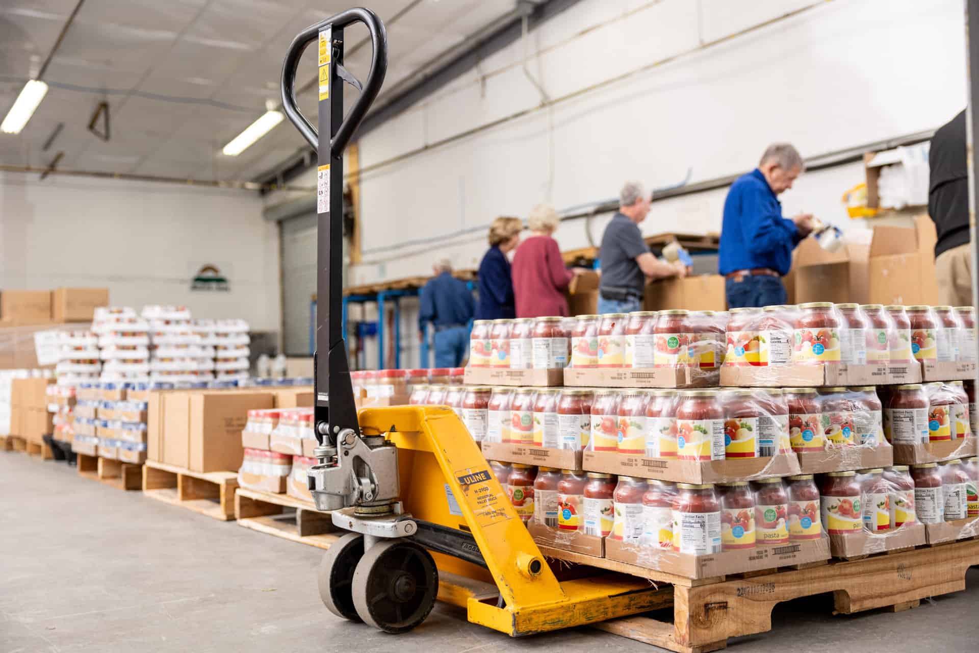A group of people working in a warehouse with pallets of food.