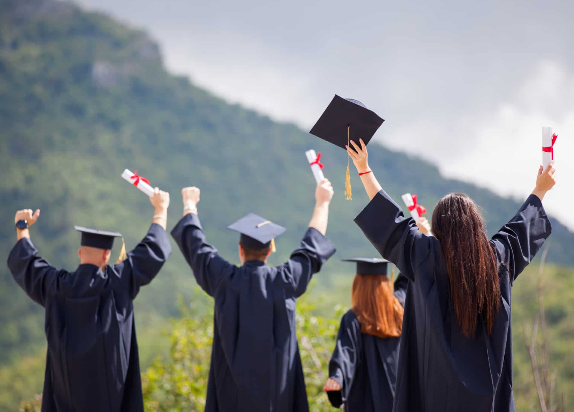 Portrait,Of,Happy,Students,In,Graduation,Gowns,Holding,Diplomas,On A group of graduates raising their hats in the air after getting their scholarships.