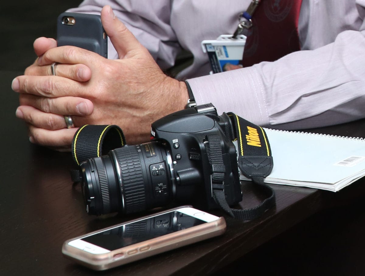 person holding phone sitting at a desk with camera and notebook on it