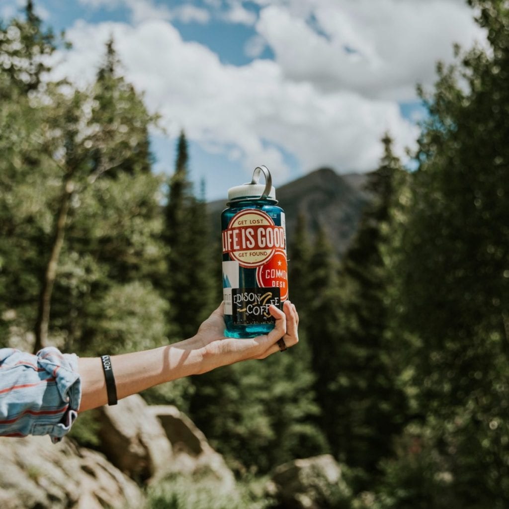 hand holding water bottle with mountains and trees in background
