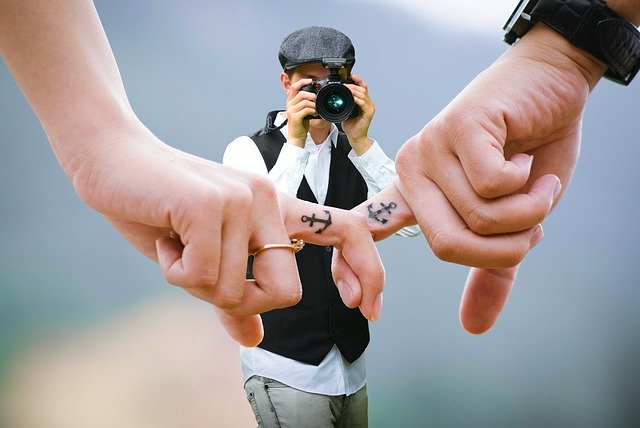 Everything You Need to Know About Wedding Photographers photographer taking a picture of two people linking fingers with anchor tattoos