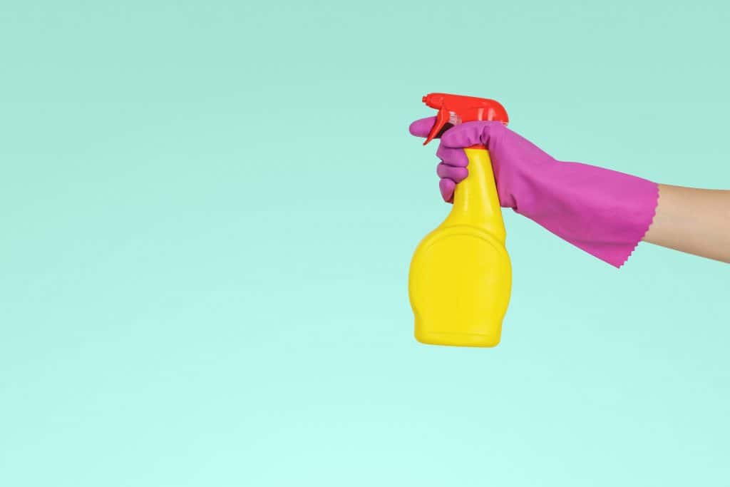 Cleaning home with yellow and red spray bottle and pink gloves.