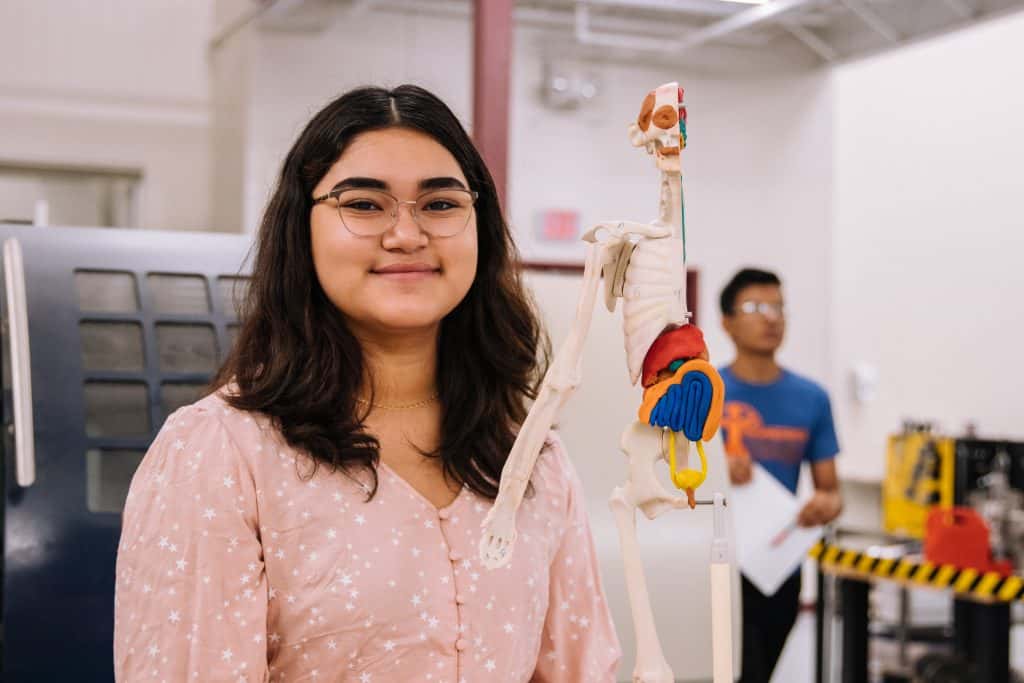 Studying to become a teacher in science, a woman poses next to an clay skeleton.