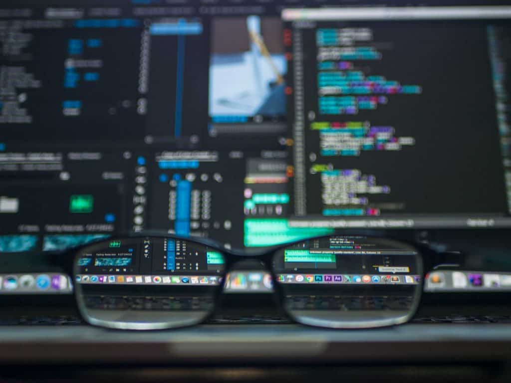 A pair of black glasses in front of a blurred hacker screen
