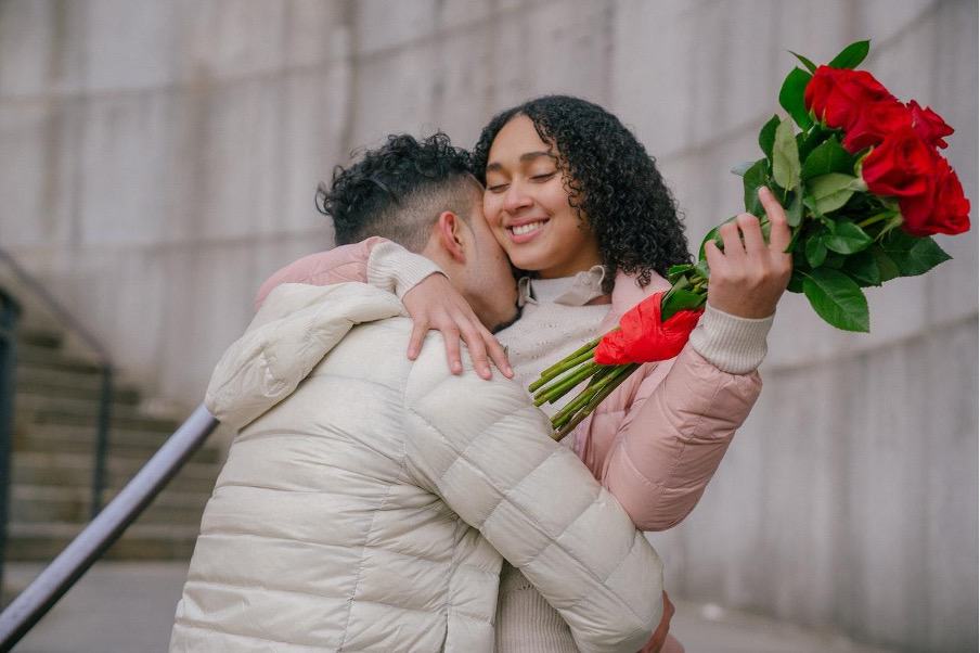 A couple hugging with a woman holding red roses
