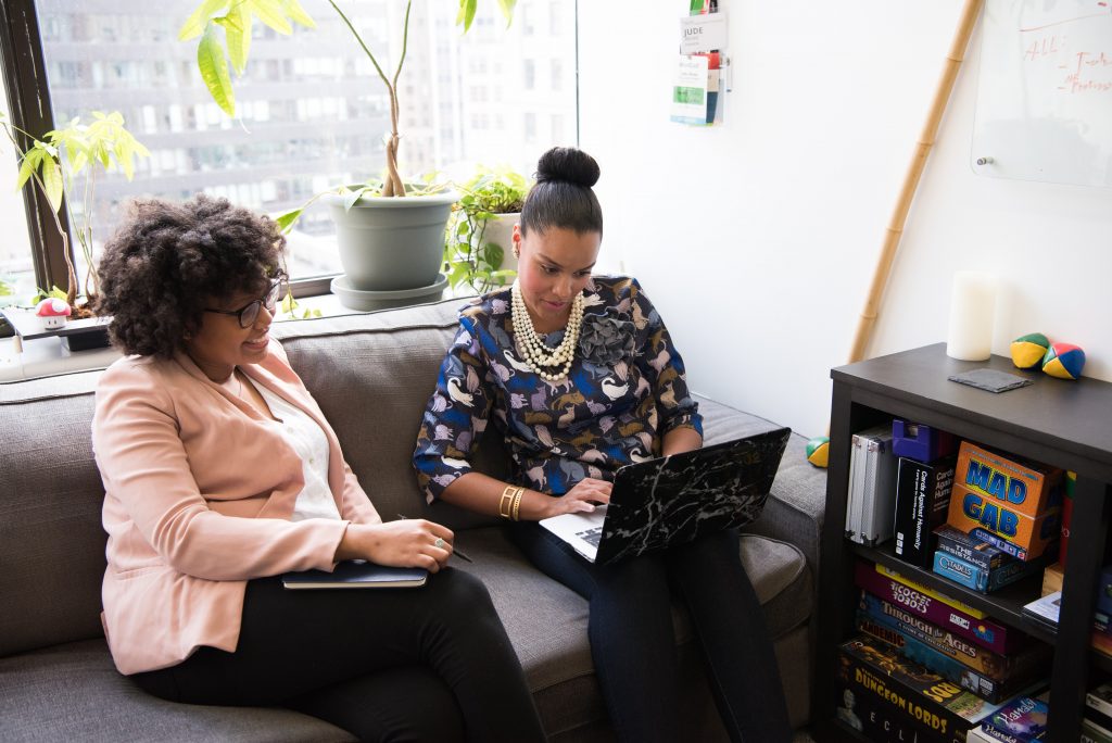 Two women working together on a laptop while sitting on a couch