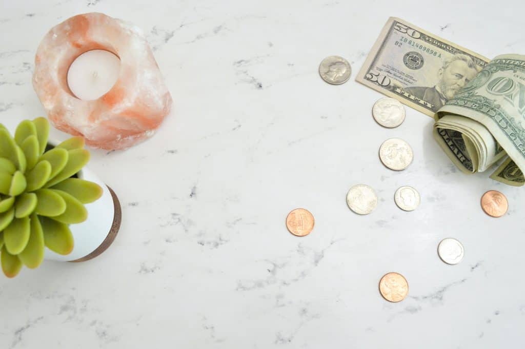 Dollars, change, a salt candle, and a succulent all sitting on a marble table.