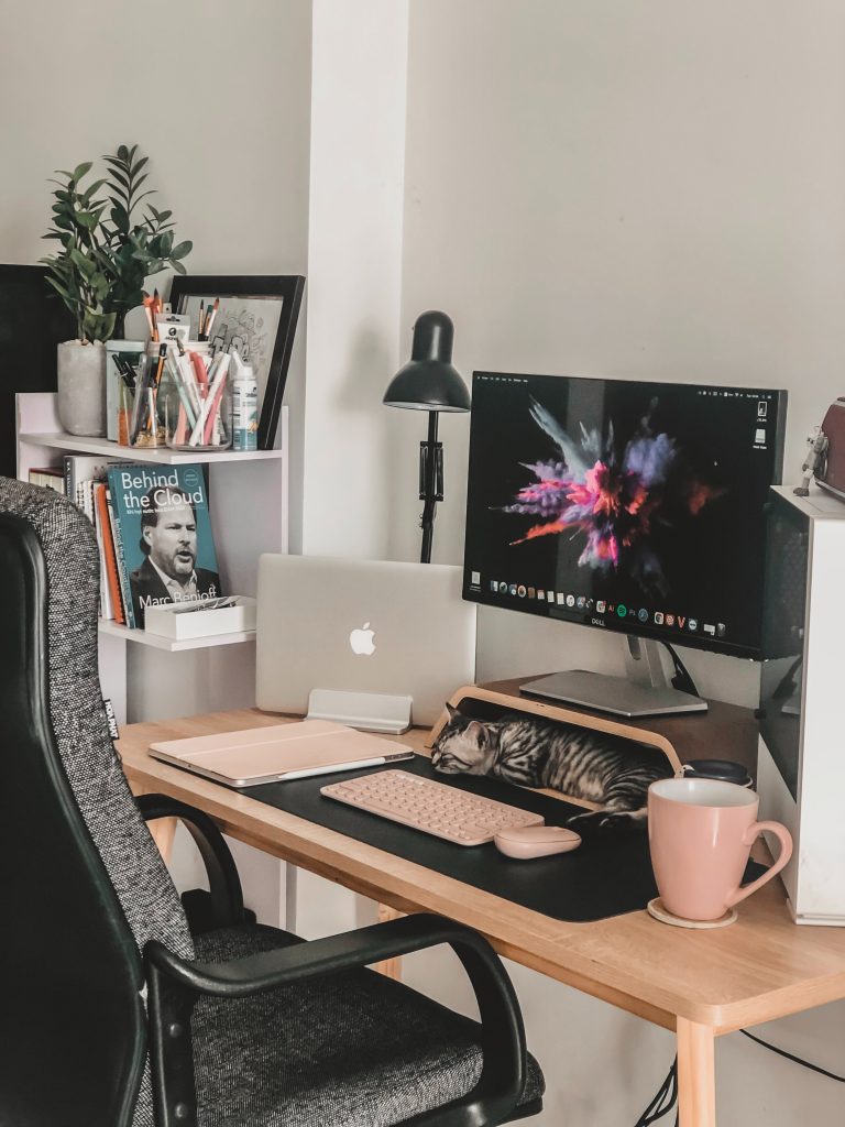 A pink work area with a kitten sleeping under the computer stand