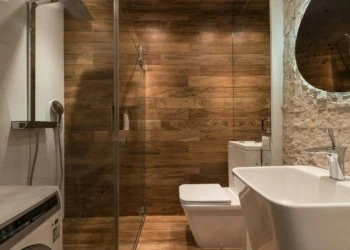 Stylish modern bathroom interior design with glass shower enclosure toilet bowl and sink under oval mirror