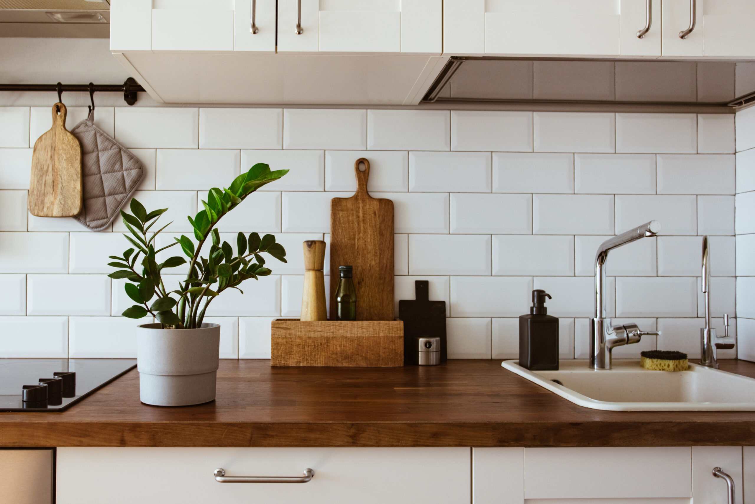 Kitchen Brass Utensils Chef Accessories. Hanging Kitchen with White Tiles Wall and Wood Tabletop.Green Plant on Kitchen Background scaled