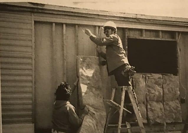 Worker installing insulation batt into mobile home wall