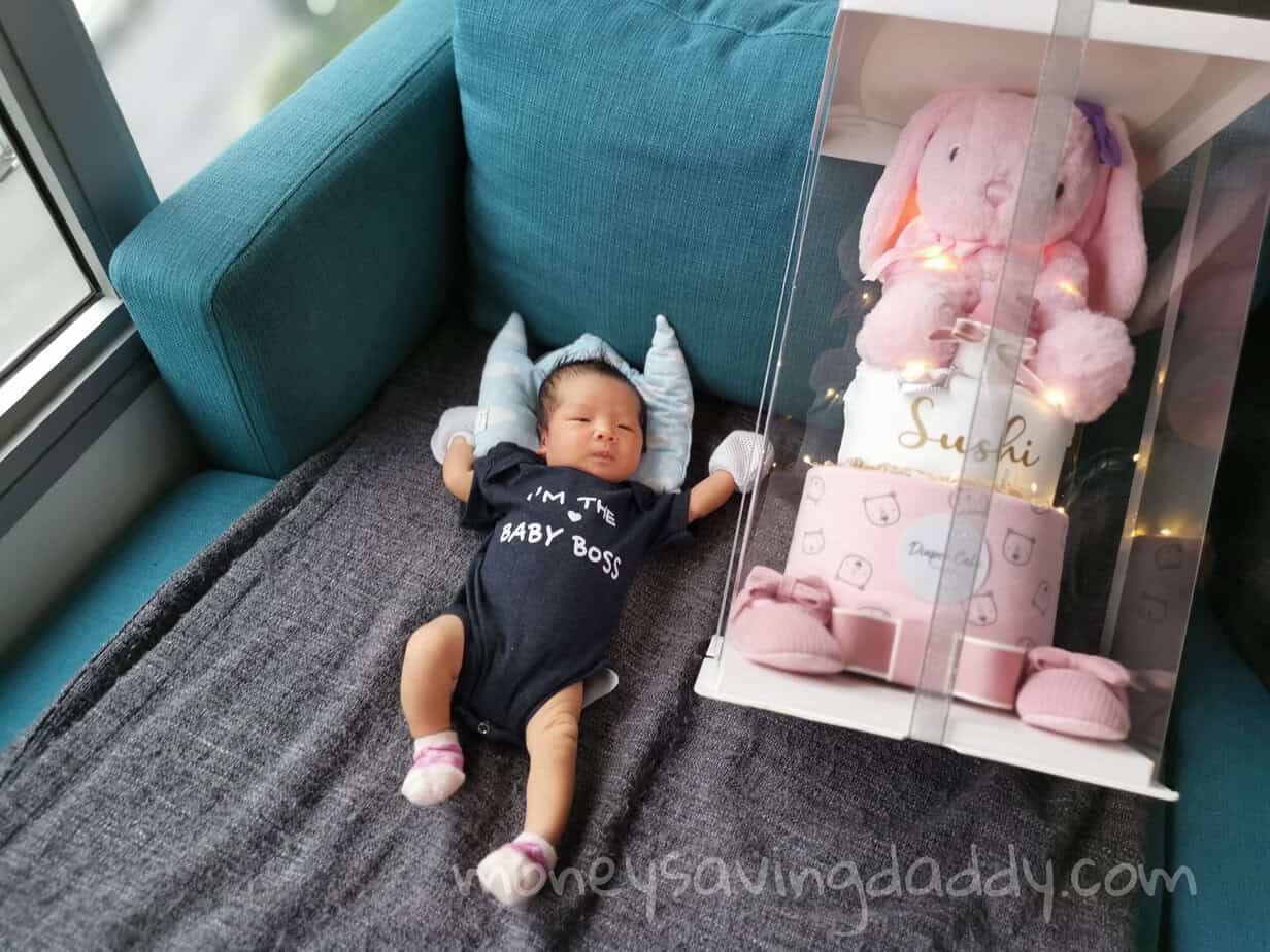 Cute baby lying on sofa with plush bunny and gift box, celebrating a special occasion.