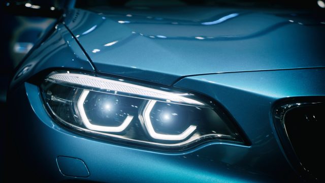 Car headlight and hood of powerful sports blue car with blue glare on dark background. Close up at Car headlight.