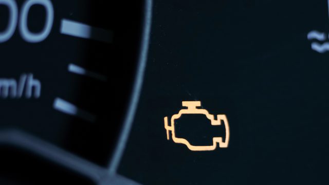 Yellow lit engine error sign on car dashboard close up