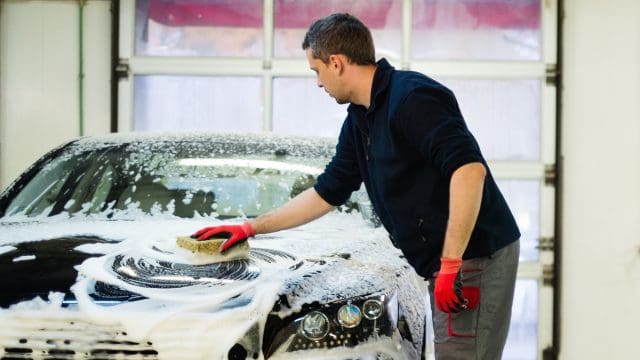 Man worker washing luxury car with sponge on a car wash
