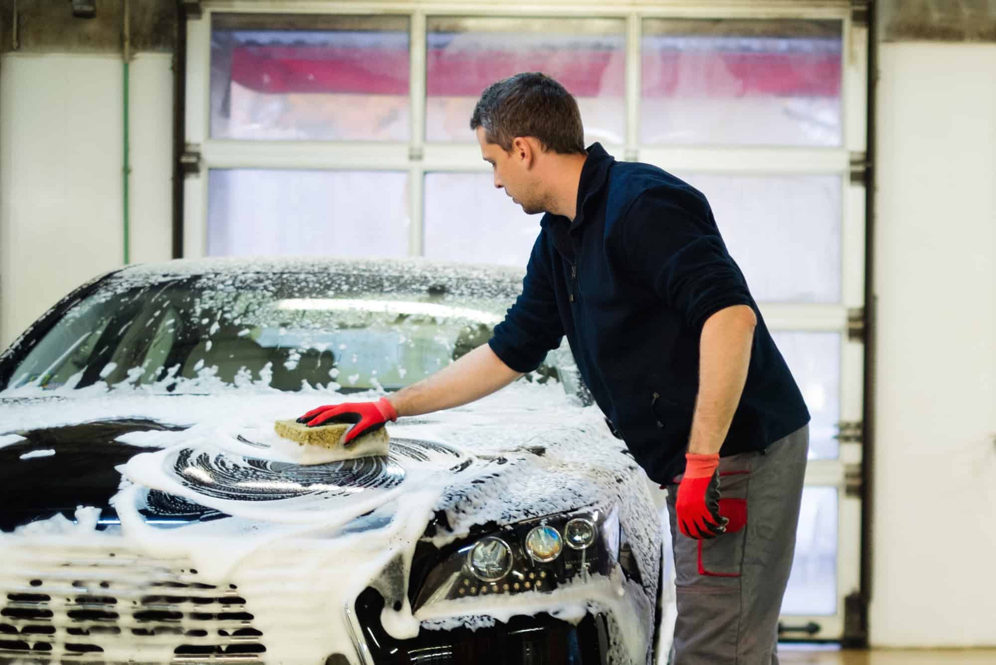 Man worker washing luxury car with sponge on a car wash