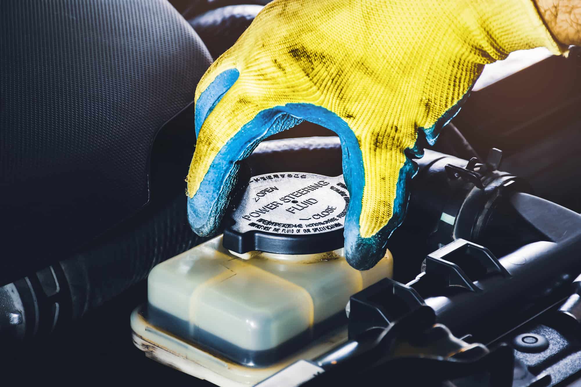 A mechanic is opening the cap of the power steering fluid to check the hydraulic fluid level